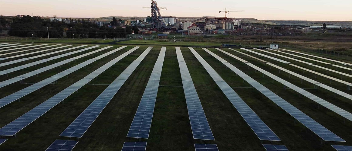 Rows of solar panels at Evander are in the foreground with a large mine complex in the background.