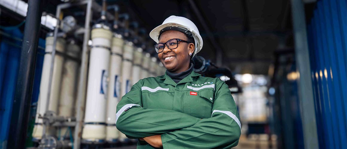 A smiling mine worker in green PPE and rows of tubes in the background.