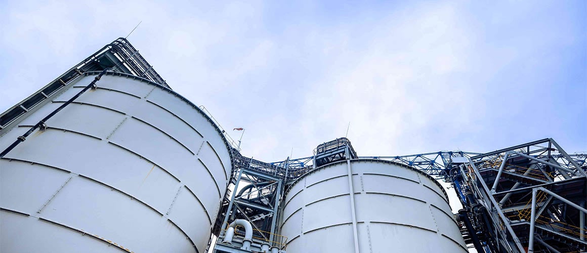 Two large silver industrial tanks or silos at Elikhulu, with a blue sky and white clouds in the background.